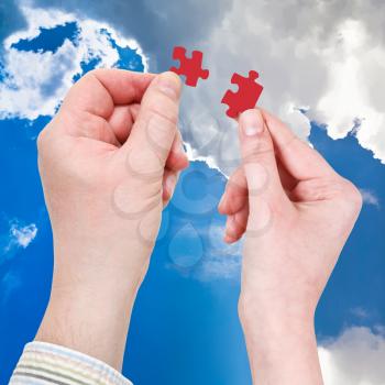 male and female hands with red puzzle pieces with blue afternoon sky background