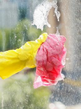 hand in yellow rubber glove washing window glass by foamy water