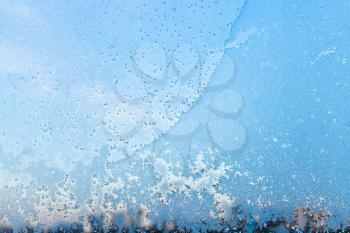 window pane with snowflakes and frost pattern in cold winter day