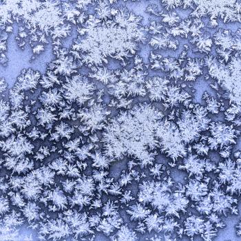 snowflakes and frost on frozen window in cold winter evening close up