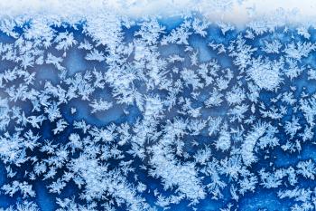 blue snowflakes and frost pattern on window in cold winter evening