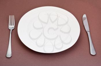 empty white plate with fork and knife set on brown background