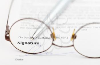 signature of sales contract and silver pen through eyeglasses