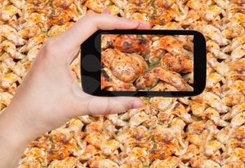 photographing food concept - tourist taking photo of roasted spicy chicken wings on hot tray on mobile gadget