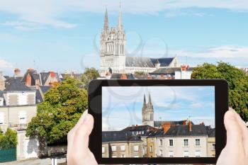 travel concept - tourist takes picture of urban houses and Saint Maurice Cathedral in Angers, France on smartphone,