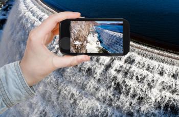 travel concept - tourist takes picture of river waterfall on Croton Dam in winter day on smartphone, USA