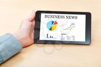 businessman hand hold tablet PC with business news on screen at office desk
