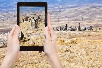 travel concept - tourist takes picture of standing menhirs of Zorats Karer (Carahunge) - pre-history megalithic monument in Armenia on tablet pc
