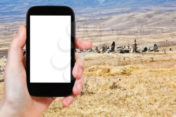 travel concept - tourist photograph view of Zorats Karer (Carahunge) - pre-history megalithic monument in Armenia on smartphone with cut out screen with blank place for advertising logo