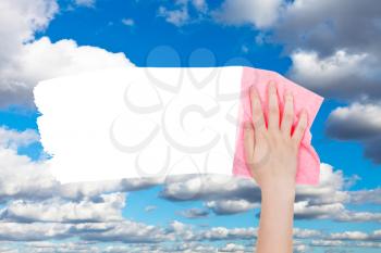weather concept - hand deletes white clouds on blue sky by pink rag from image and white empty copy space are appearing