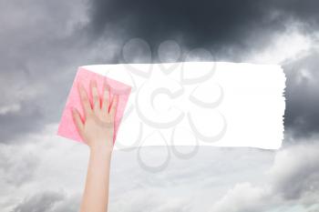 weather concept - hand deletes gray clouds from sky by pink rag from image and white empty copy space are appearing