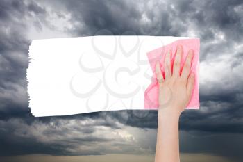 weather concept - hand deletes storm clouds on sky by pink rag from image and white empty copy space are appearing