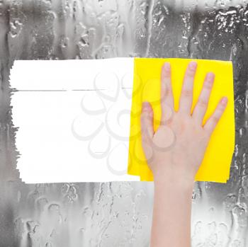 weather concept - hand deletes rainy water on window by yellow rag from image and white empty copy space are appearing