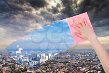 ecology concept - hand deletes dirty city by pink cloth from image and clear blue cityscape is appearing