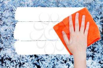 weather concept - hand deletes winter frozen texture on glass by orange rag from image and white empty copy space are appearing
