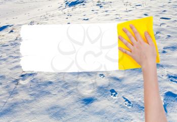 season concept - hand deletes snow surface by yellow rag from image and white empty copy space are appearing