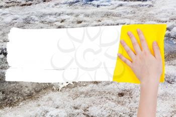 weather concept - hand deletes melting snow by yellow rag from image and white empty copy space are appearing