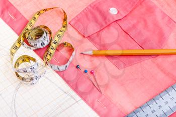 dressmaking still life - top view of cutting table with pattern, measure tape, pencil, pins, red shirt