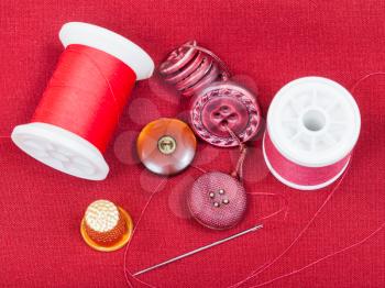 dressmaking still life - top view of bobbins with sewing thread, buttons, thimble, needle on red tissue