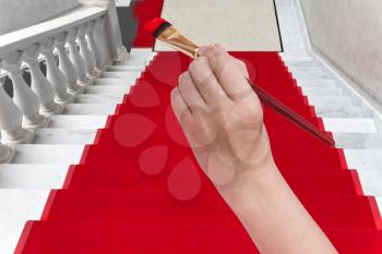 art concept - hand with paintbrush paints red carpet on white marble staircase