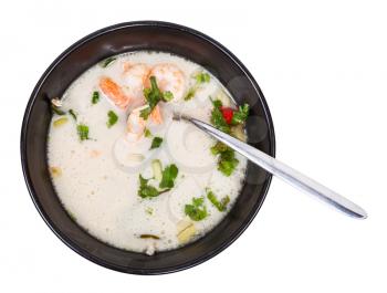 top view of sour and spicy soup Tom yam nam khon made with shrimps, coconut milk, chilli pepper, lemongrass, galangal, coriander, kaffir lime leaves in bowl isolated on white background