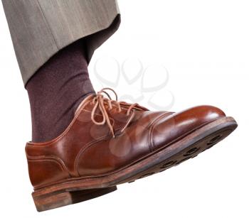 male right foot in brown shoe takes a step isolated on white background