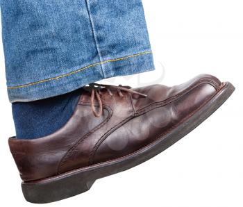 side view of male right foot in jeans and brown shoe takes a step isolated on white background