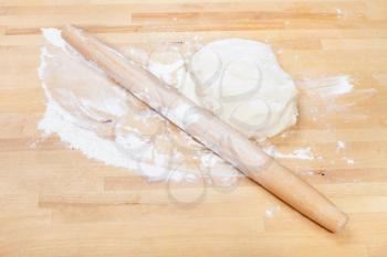 flour, rolling pin and piece of raw dough on wooden table