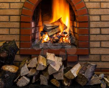 stack of wood and burning wood in indoor brick fireplace in country cottage