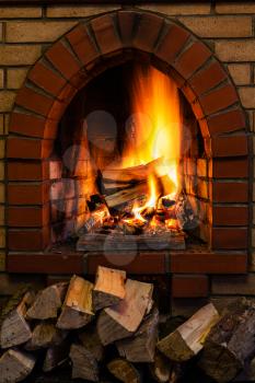 wood stack and logs burning in indoor brick fireplace in country cottage