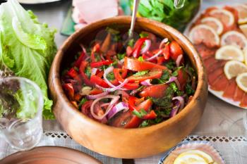 salad from fresh tomatoes, cucumbers, red onion seasoned by olive oil in wooden bowl on served table
