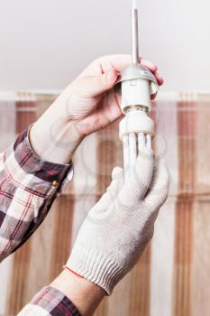 Electrician changing compact fluorescent lamp in lampholder in room