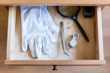 above view of magnifier, forceps and white gloves in open drawer of nightstand