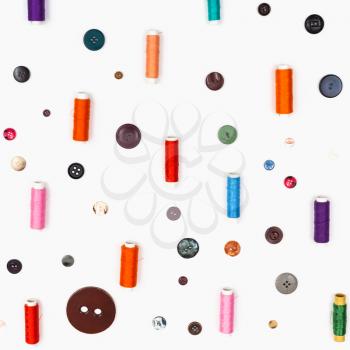 spools of sewing thread and various buttons on square white background