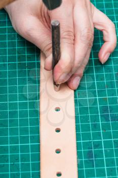 punching holes in new leather belt with hole punch on self-healing mat