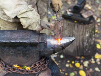 Blacksmith processing red hot iron rod on anvil in outdoor rural smithy