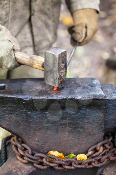 Blacksmith forges hot iron rod with sledgehammer on anvil in outdoor rural smithy