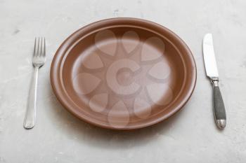 food concept - brown plate with knife, spoon on gray concrete surface