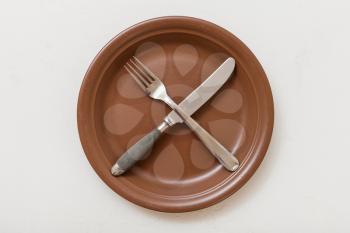 food concept - top view of brown plate with crossing knife, spoon on white plastering board