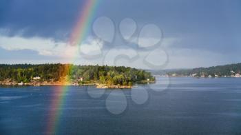 above view of green island with settlement in Baltic Sea and rainbow over water in sunny autumn day, Sweden
