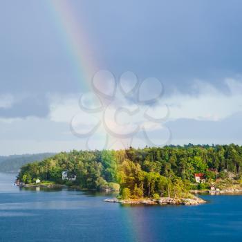 green island with village in Baltic Sea and rainbow in blue sky in sunny autumn day, Sweden