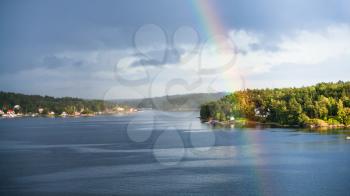 above view of green coast of Baltic Sea with settlements and rainbow over water in sunny autumn day, Sweden