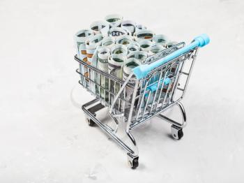 shopping carriage with rolls from dollar banknotes on concrete board