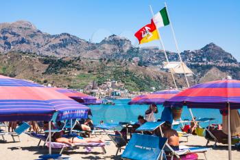 GIARDINI NAXOS, ITALY - JULY 8, 2011: flags over people on urban beach of Giardini Naxos town. Naxos was founded by Thucles the Chalcidian in 734 BC, and since 1970s it has become a seaside-resort