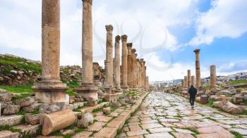 Travel to Middle East country Kingdom of Jordan - tourist on Cardo Maximus road in Jerash (ancient Gerasa) town in winter in rain