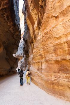 PETRA, JORDAN - FEBRUARY 21, 2012: tourists walk in Al Siq passage to ancient Petra town in winter. Rock-cut town Petra was established about 312 BC as the capital city of the Arab Nabataean