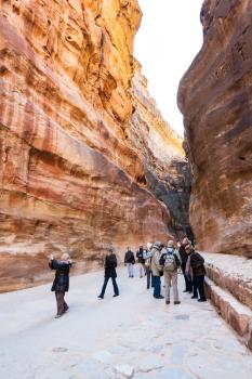 PETRA, JORDAN - FEBRUARY 21, 2012: tourists in Al Siq pass to ancient Petra town in winter. Rock-cut town Petra was established about 312 BC as the capital city of the Arab Nabataean