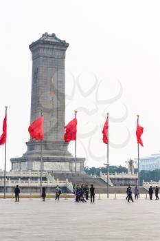 BEIJING, CHINA - MARCH 19, 2017: tourists and red flags near Monument to the People's Heroes on Tiananmen Square in spring. Tiananmen Square is central city square in Beijing