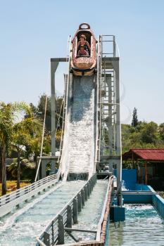 riders in boat on water slide attraction in summer day