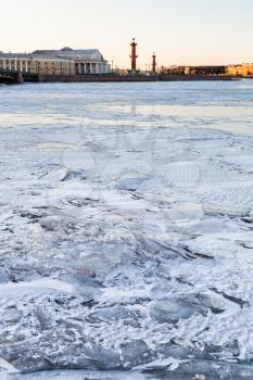 ice-bound Neva river and Spit of Vasilyevsky Island with Rostral Column and Old Stock Exchange building in Saint Petersburg city in March evening